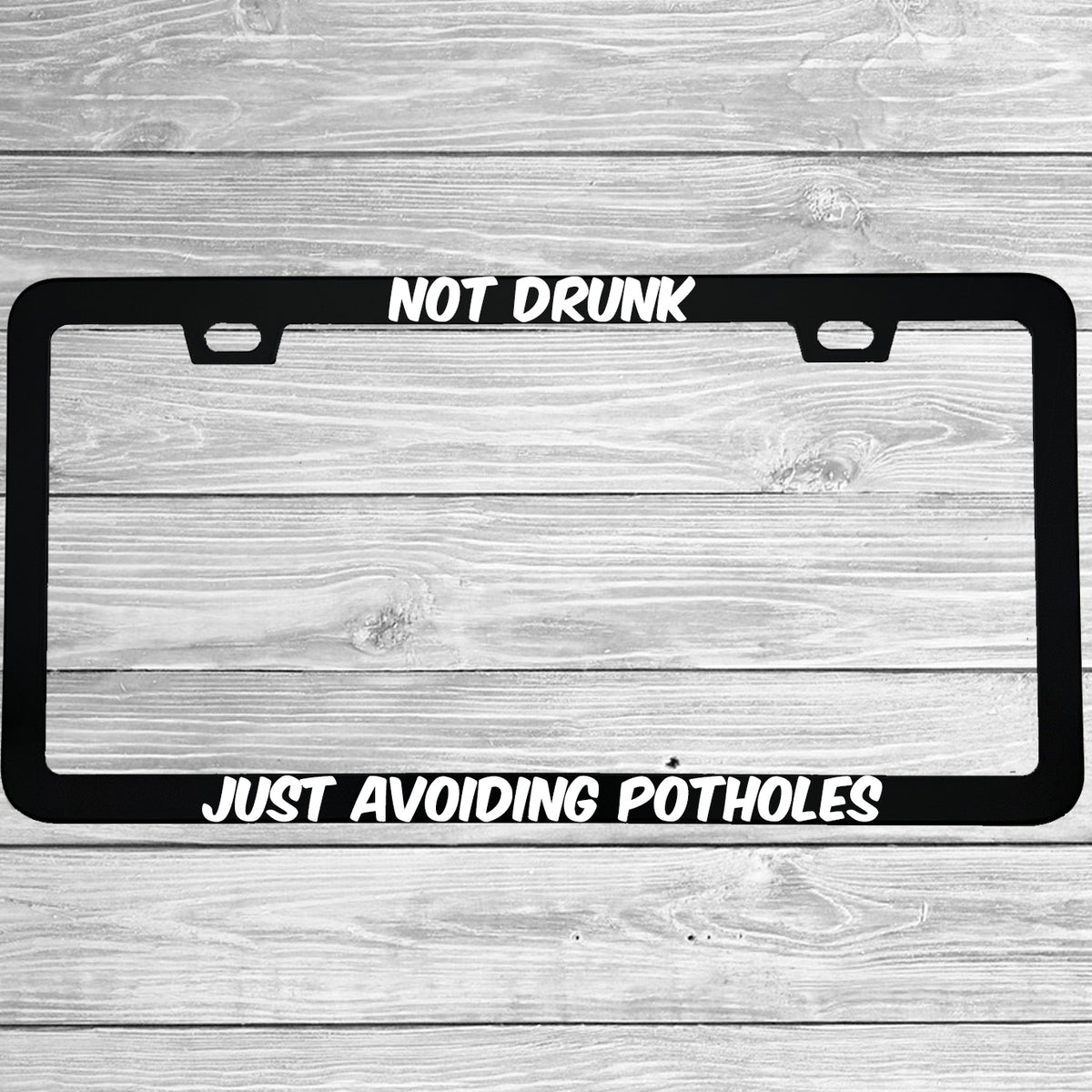 Close-up of "Not Drunk Just Avoiding Potholes" license plate frame showing fade-proof print quality