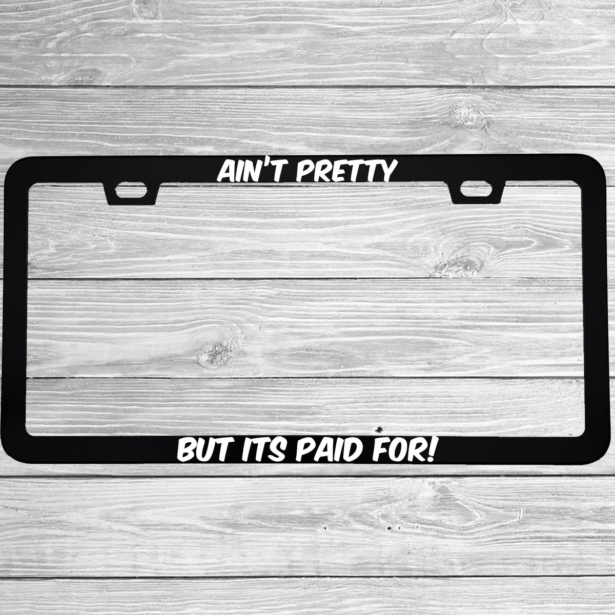 Close-up of "Ain't Pretty But Its Paid For" license plate frame showing fade-proof print quality