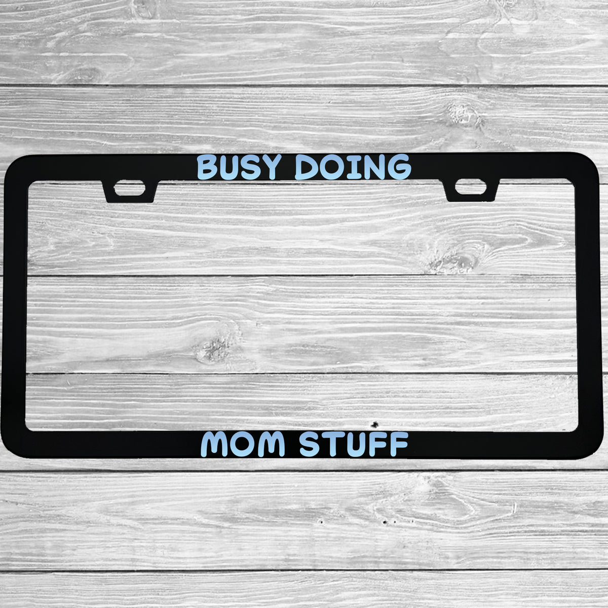 Close-up of "Busy Doing Mom Stuff" license plate frame showing fade-proof print quality